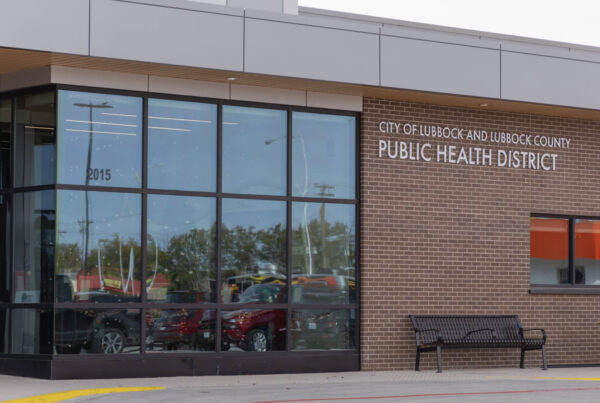 City of Lubbock and Lubbock County Public Health District building with large glass windows, brick facade, and a black bench outside.