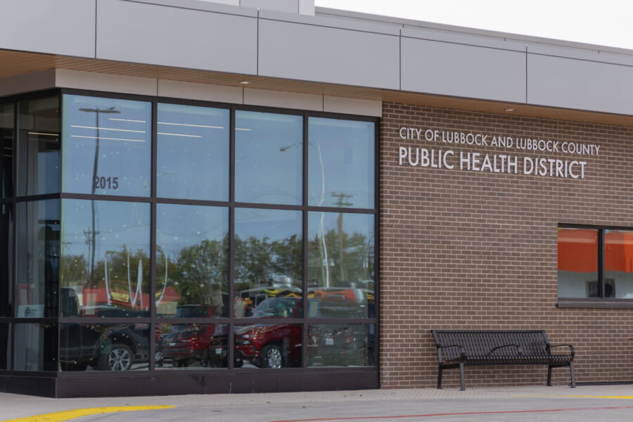 City of Lubbock and Lubbock County Public Health District building with large glass windows, brick facade, and a black bench outside.