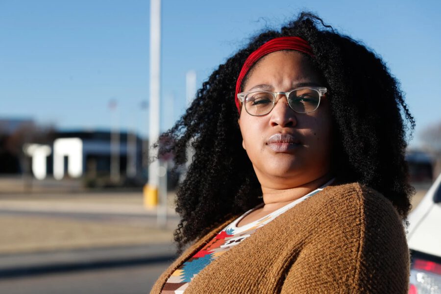 A woman standing outdoors in Lubbock, Texas, wearing a red headband and glasses, looking determined. The image relates to a Texas Tribune article discussing racism and antisemitism in local schools.